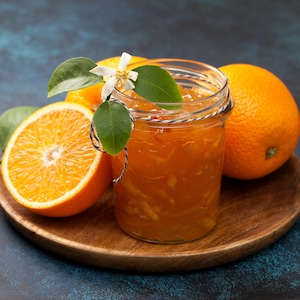 Un pot de marmelade d'orange dans un pot en verre, entouré d'une moitié d'orange et de deux oranges entières.