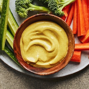 Il y a un petit bol de mayo au cari dans une grande assiette de crudités.