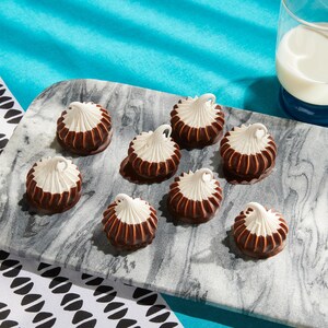Des meringues trempées dans le chocolat sur une planche à découper.