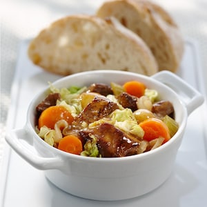 Un bol de mijoté de boeuf, de chou et de légumes, servi avec des tranches de pain croûté frais.