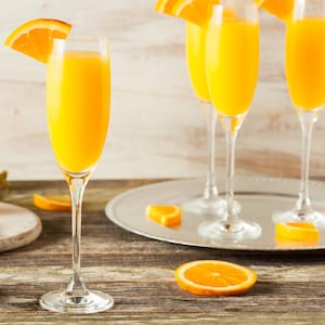 Une flûte à champagne remplie de mimosa et trois autres flûtes remplies en arrière plan avec une bouteille de champagne.