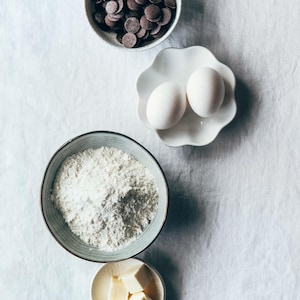 Les ingrédients principaux pour le moelleux au chocolat, dans des petits bols, dont du beurre, de la farine, des oeufs et des pastilles de chocolat.