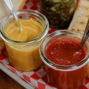 Des pots de moutarde et de ketchup servis dans un cabaret, aux côtés de pains à hot-dog et de relish.