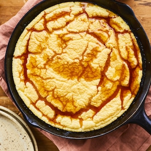 Omelette soufflée garnie de sirop d'érable dans un poêlon en fonte déposé sur un linge de table à coté de deux assiettes empilées. 