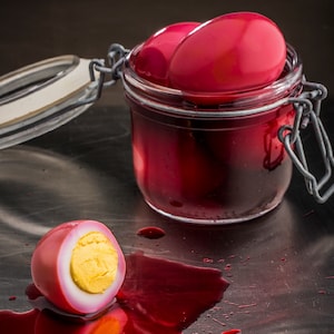 Un pot de verre avec des œufs au vinaigre de betterave rouges.