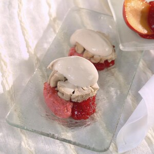 Deux boules de sorbet rose foncé recouvertes d'une tranche de cervelle de veau et d'une quenelle de crème sure, dans une assiette en verre.  