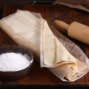 Une pâte feuilletée avec un rouleau à pâte et un bol de farine.