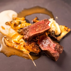Deux morceaux de viande de cerf cuit disposés dans une assiette et garnis d'une sauce aux champignons.