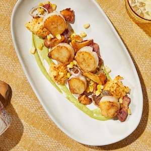 Pétoncles poêlés, petits pois, maïs et champignons dans une assiette avec une purée de petits pois au bacon.