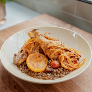 Des pilons de poulet sur un nid de lentilles vertes tomatées.