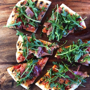 Une pizza au prosciutto et à la roquette sur une planche en bois.