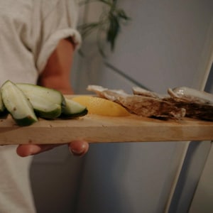 Quelqu'un présente une planche de bois avec des morceaux de tomates, de concombres et des huîtres.