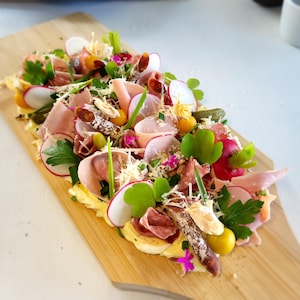 Une planche à découper contenant du beurre, du jambon, des charcuteries, des légumes et des fines herbes.