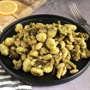 Une assiette de gnocchis au pesto et au brocoli avec une tranche de citron et une fourchette.