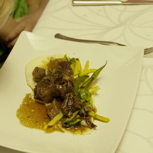 Une assiette de poitrine de porc croustillante et de légumes déposée sur une table devant un enfant.