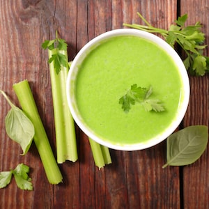 Un bol rempli de potage purée de céleri et des branches de céleri à côté.