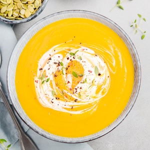 Un potage à la courge décoré de pousses et de crème.