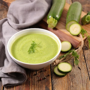 Un bol rempli de potage aux courgettes avec une planche à découper recouverte de courgettes.