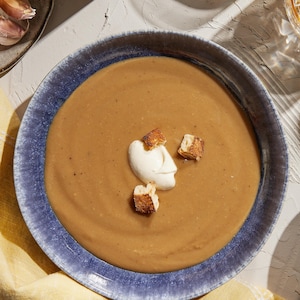 Potage garni de crème aux croûtes de parmesan et croûtons de baguette dans un bol.