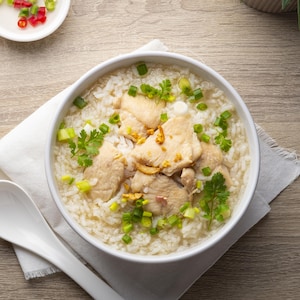Un bol de potage de riz garni de tranches de poulet, d'oignons verts et de coriandre.