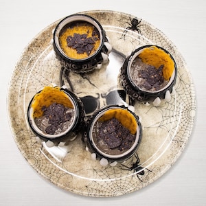 Quatre petits pots en forme de chaudron de sorcière remplis de potage aux haricots noir et à la bière dans une assiette au thème de l'Halloween.