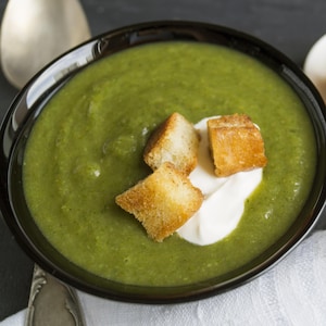 Un bol de potage vert avec trois croûtons et un peu de crème en guise de décoration.