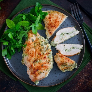 Une poitrine de poulet rôtie entière et une poitrine coupée en tranche dans une assiette avec des fines herbes.