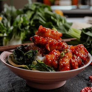 Du poulet général Tao servi sur un lit de riz et aux côtés de bok choys.