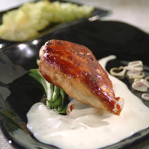 Un morceau de poulet sur une bonne quantité de sauce blanche dans une assiette noire.