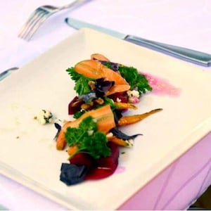 De la salade aux carottes rôties, betteraves et fromage de chèvre déposée dans une assiette blanche.