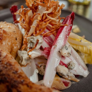 Une salade d'endives, fromage bleu et chips de salsifis dans une assiette à côté de poulet en crapaudine.