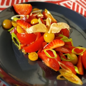 Une salade de fruits sur une assiette noire et nappe rouge.