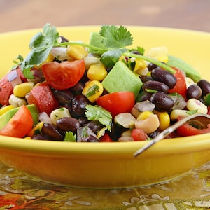 Un bol de salade mexicaine contenant des fèves noires, du maïs en grain, des tomates ainsi que de la coriandre fraîche.