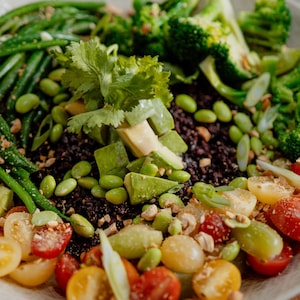 Un salade de riz noir garnie de petites tomates, de haricots verts, de brocolis et d'edamames.