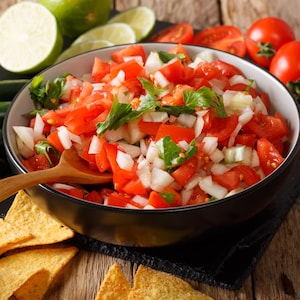 Un bol de salsa de tomates avec des croustilles, de la lime, des tomates entières et des jalapenos.