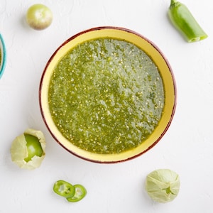 Des bols contenant de la salsa verde entourés de tomatillos et de piment jalapeños.