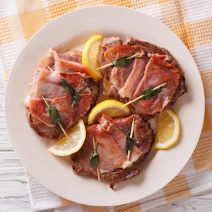 Une assiette de saltimbocca avec des quartiers de citron.