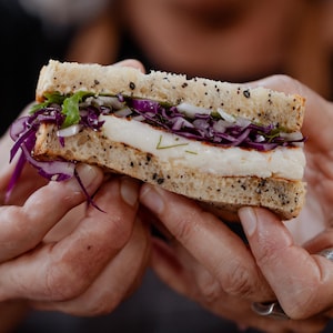 Une part de sandwich au fromage, salade de chou rouge et fenouil dans les mains de la cheffe Josée Robitaille.