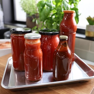 Des bouteilles en verre de différents formats remplis de sauce tomate.