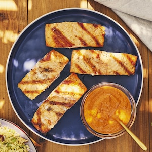 Quatre pavés de saumon grillé dans une assiette avec un bol de sauce romesco.