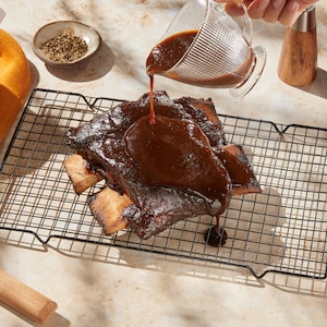 Une personne versant de la sauce brune sur un morceau de short ribs de bœuf.