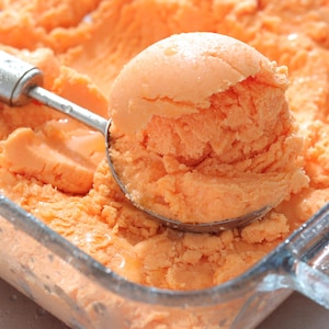 Une cuillère à crème glacée sur un plat de sorbet au cantaloup et au gingembre.