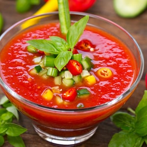 Un verre rempli de soupe froide aux tomates avec des légumes en garniture.