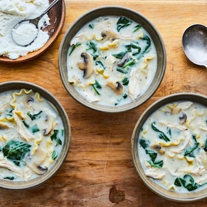 Trois bols de soupe-lasagne sur une table en bois accompagnés de ricotta.