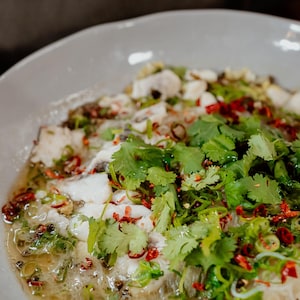 Un bol de service rempli de soupe de poisson et garni de feuilles de coriandre fraîche.