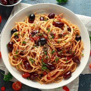 Des spaghettis recouverts de morceaux de tomates, d'olives, d'anchois et de persil.
