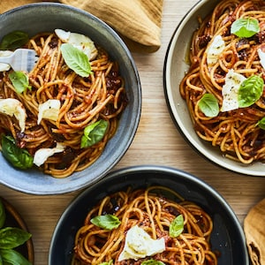 Bols de spaghetti aux tomates et au pesto posés sur une table en bois.