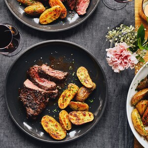 Table chic garnie de deux assiettes de steak de bison et de frites, ainsi que de bols de salade et de patates rôties, d'un vase de fleurs et de deux verres de vin.