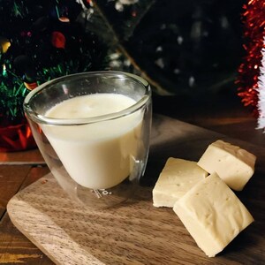 3 cubes de sucre à la crème sur une planche de bois et un verre de lait à côté.