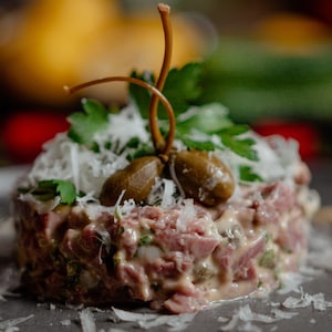 Un tartare de canard garni de fromage manchego et de feuilles de persil.
